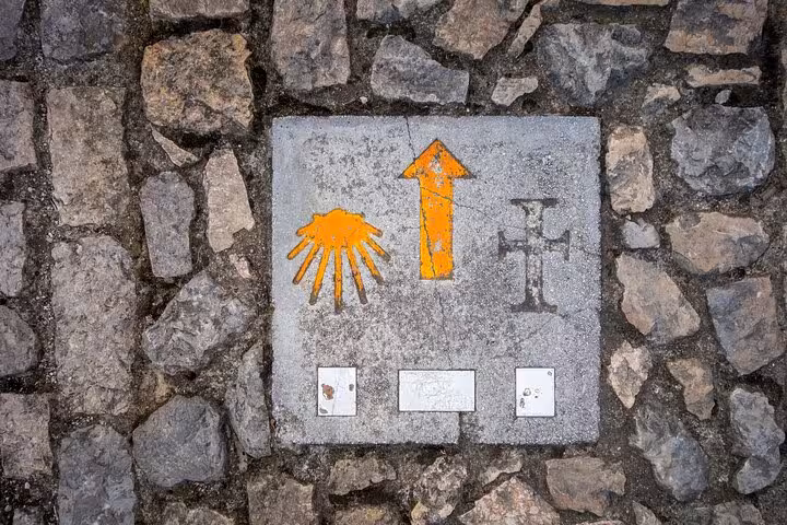 Waymarker with scallop shell symbol and arrow on the Camino de Santiago path in Santiago de Compostela.