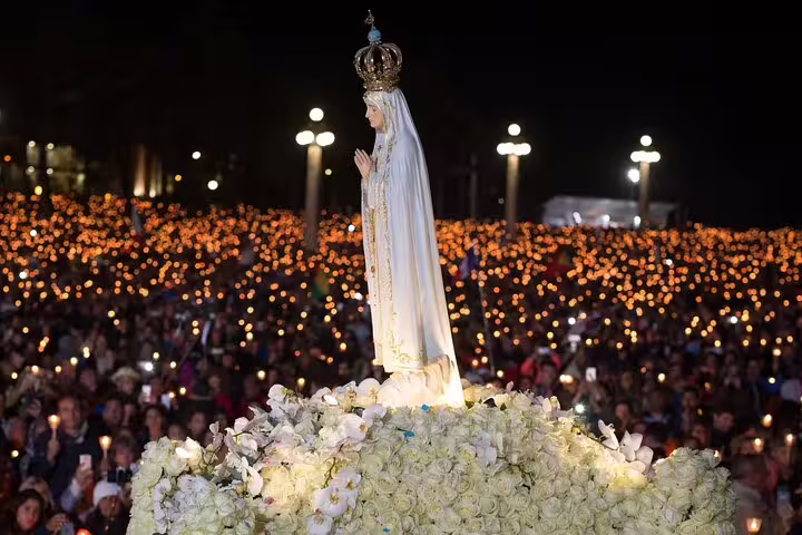 Candlelit procession at Sanctuary of Fatima, Portugal, with flowers and a statue, highlighting spiritual and cultural significance.