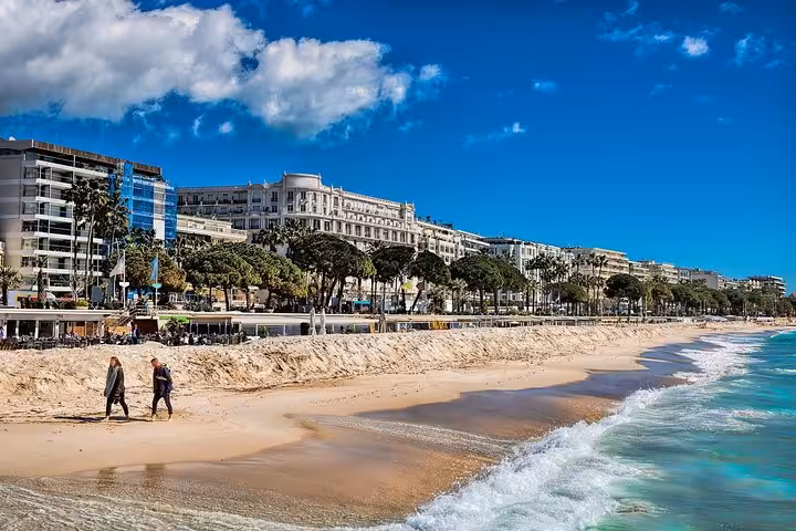 Peaceful Cannes beach with gentle waves, sandy shore, and iconic buildings along the vibrant promenade.