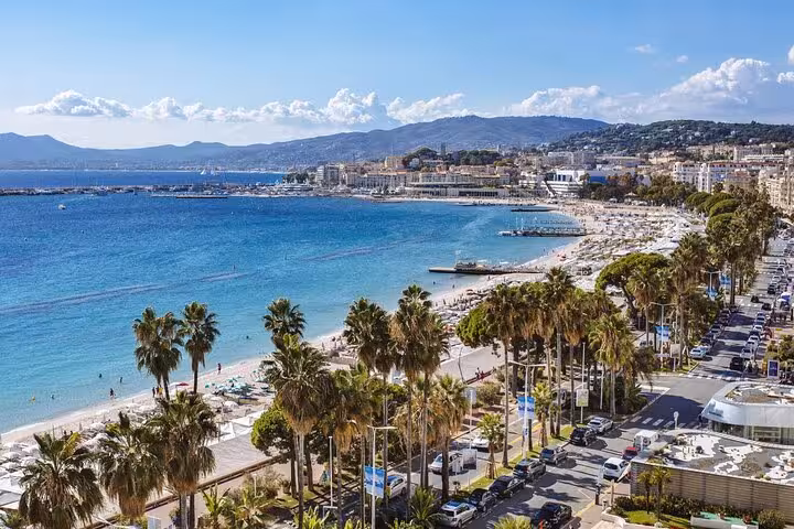 Vibrant Cannes beachfront with palm-lined promenade and azure Mediterranean waters, perfect for a coastal tour.