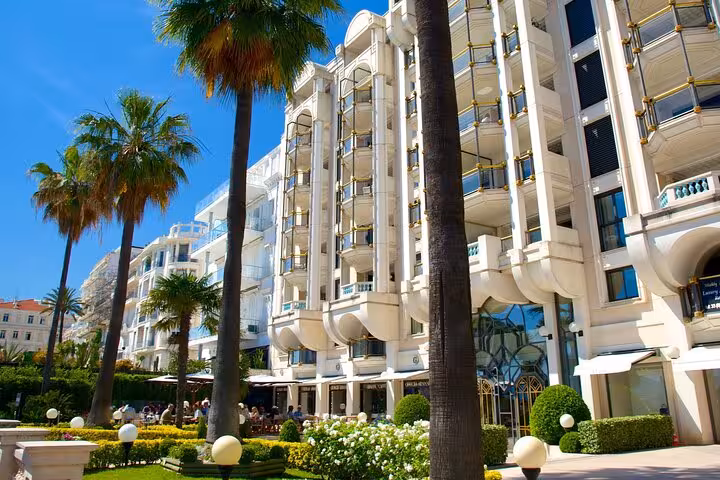 Elegant building and lush gardens with palm trees in the sunny cityscape of Cannes, France.