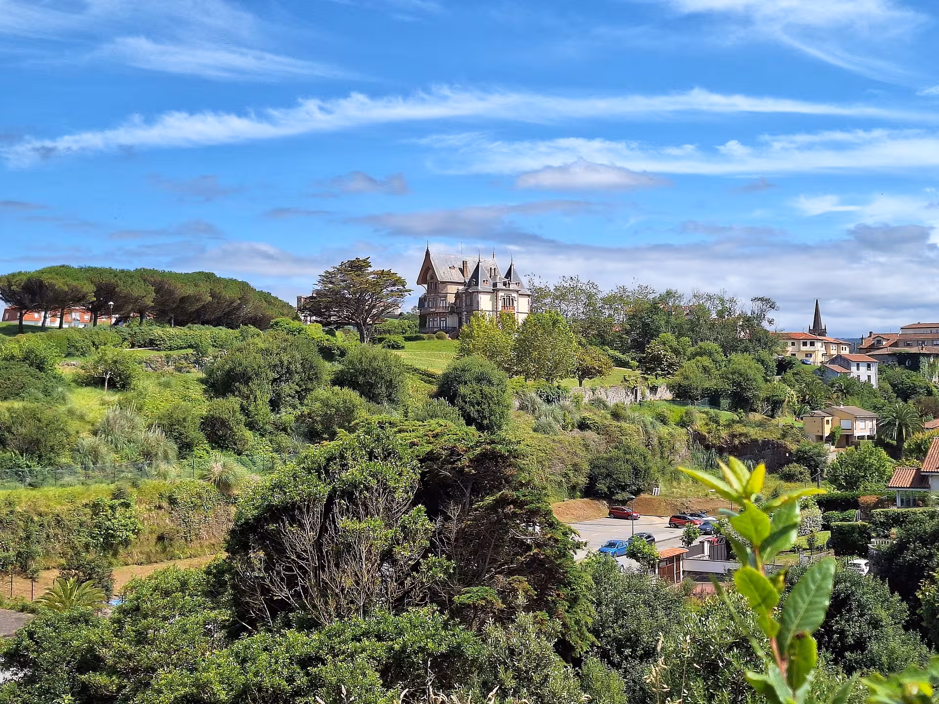 Scenic view of a historic mansion surrounded by lush greenery in Cantabria's coastal landscape under a bright sky.