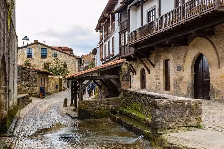 Charming cobblestone street in a Cantabrian coastal town showcasing rustic stone buildings and a quaint water feature.
