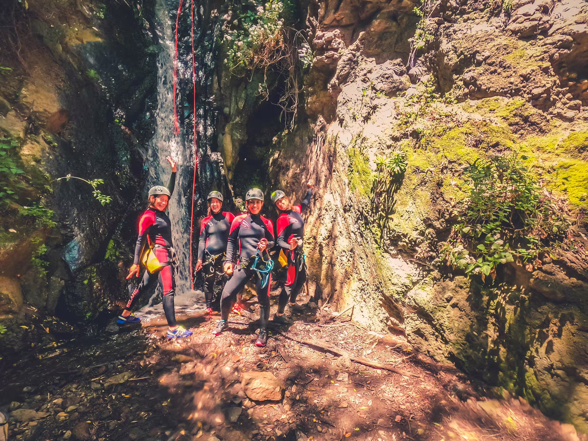 Group of canyoners in wetsuits celebrate near a waterfall on a rainforest canyoning adventure.