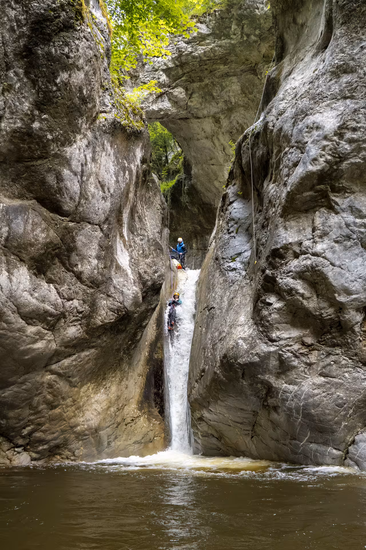 Adventurers canyoning down a narrow waterfall in Chli Schliere near Luzern, surrounded by towering rock formations.
