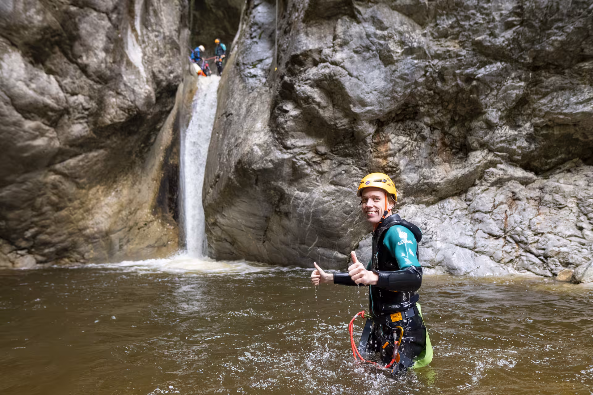 Canyoning enthusiast gives a thumbs-up in front of a waterfall at Chli Schliere, highlighting the excitement of Swiss adventure.