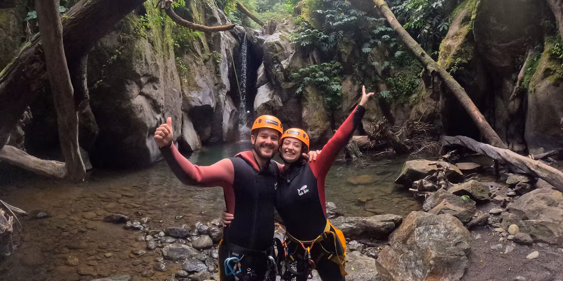 Happy canyoning couple in helmets at Salto do Cabrito waterfall pool, São Miguel Azores adventure tour