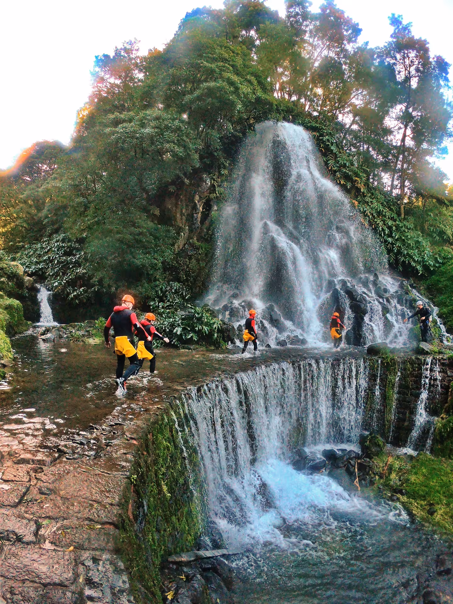 Adventure canyoning tour in Furnas Azores, participants walking beside tiered waterfalls and lush volcanic forest