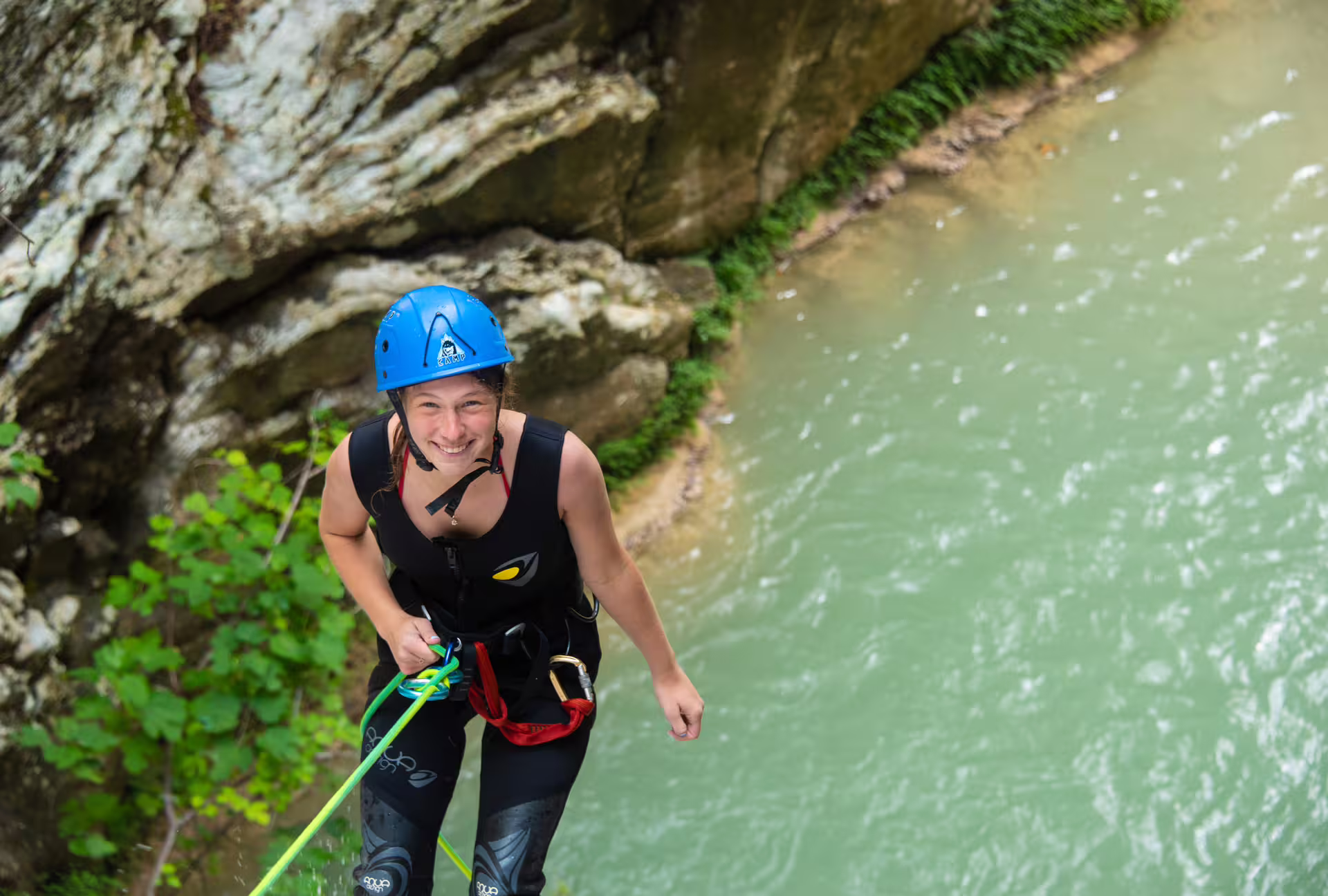 Smiling canyoning guide on rope rappel above river pool at Neda Waterfalls adventure tour, Greece