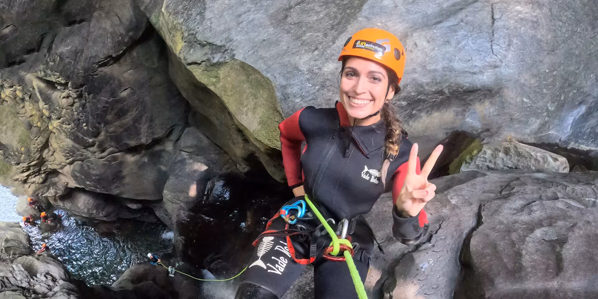 Smiling canyoning guide rappels into Salto do Cabrito gorge, São Miguel Azores, with helmet and rope