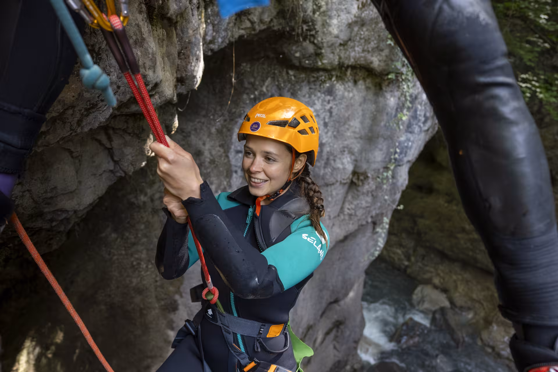 Smiling canyoning participant in Interlaken rappels down a rock face, showcasing adventure and safety gear.