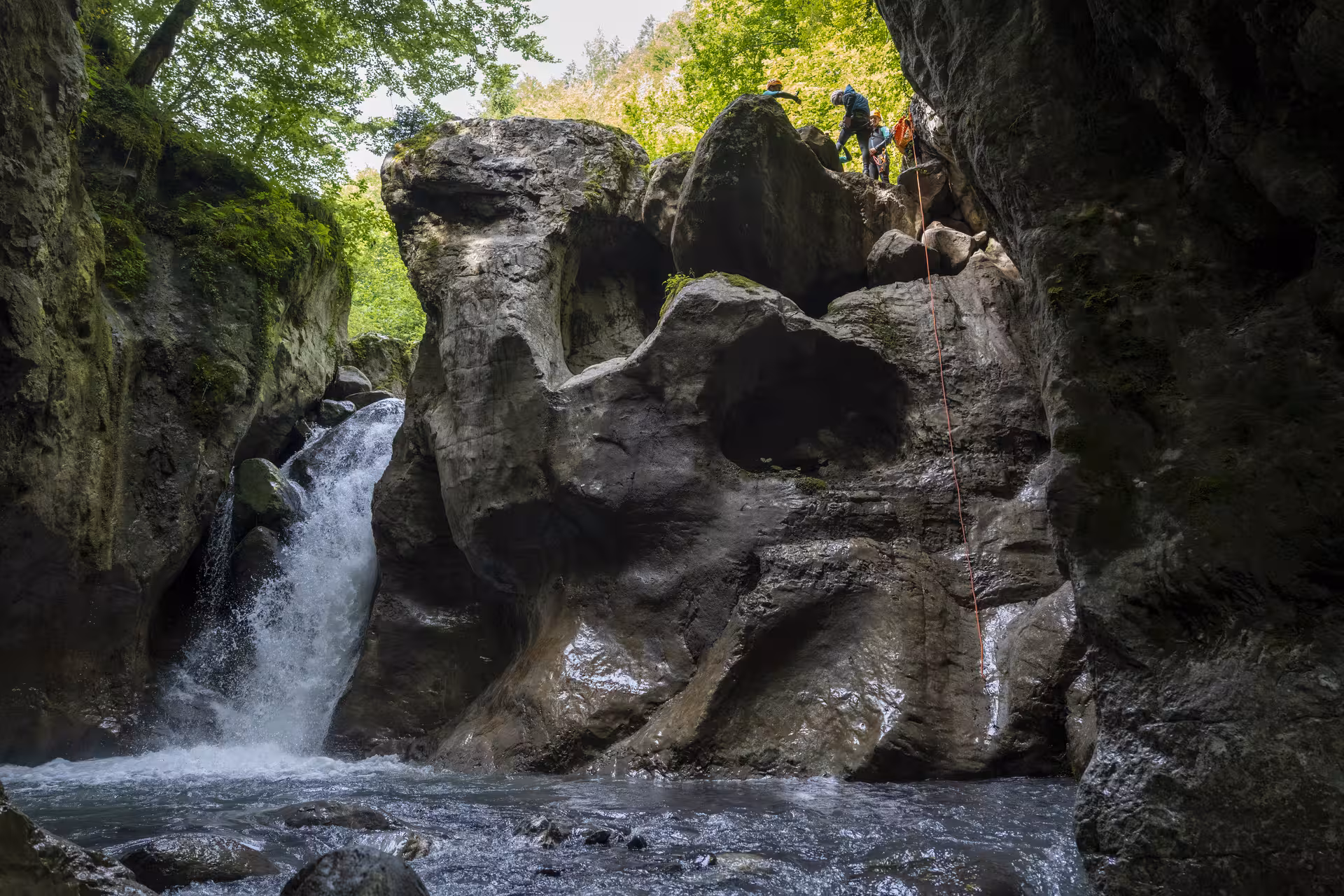 Thrilling canyoning descent in Interlaken with adventurers scaling rocky cliffs next to a waterfall.