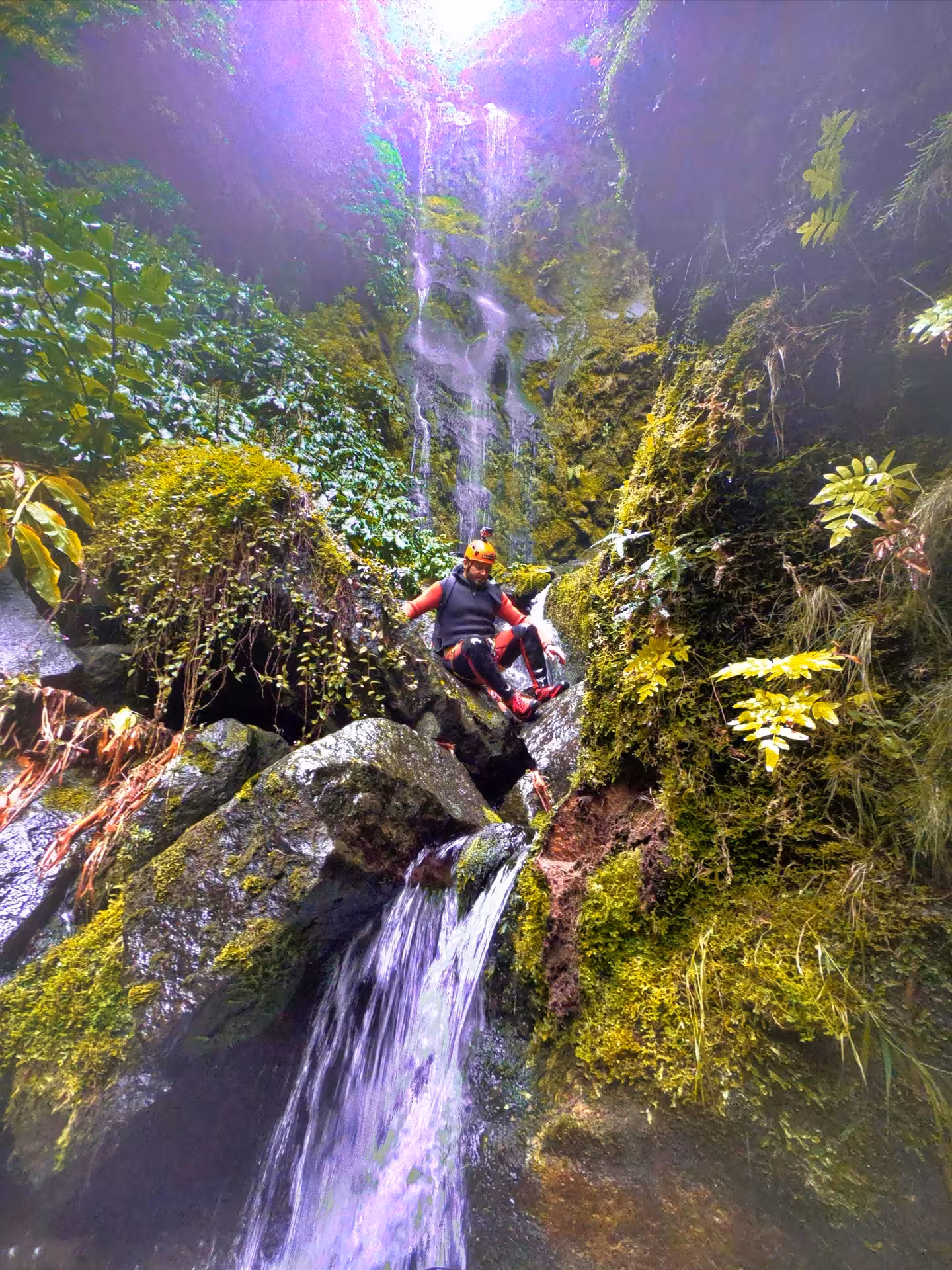 Canyoning Lombadas Praia tour with adventurer sliding down mossy rocks beside a rainforest waterfall