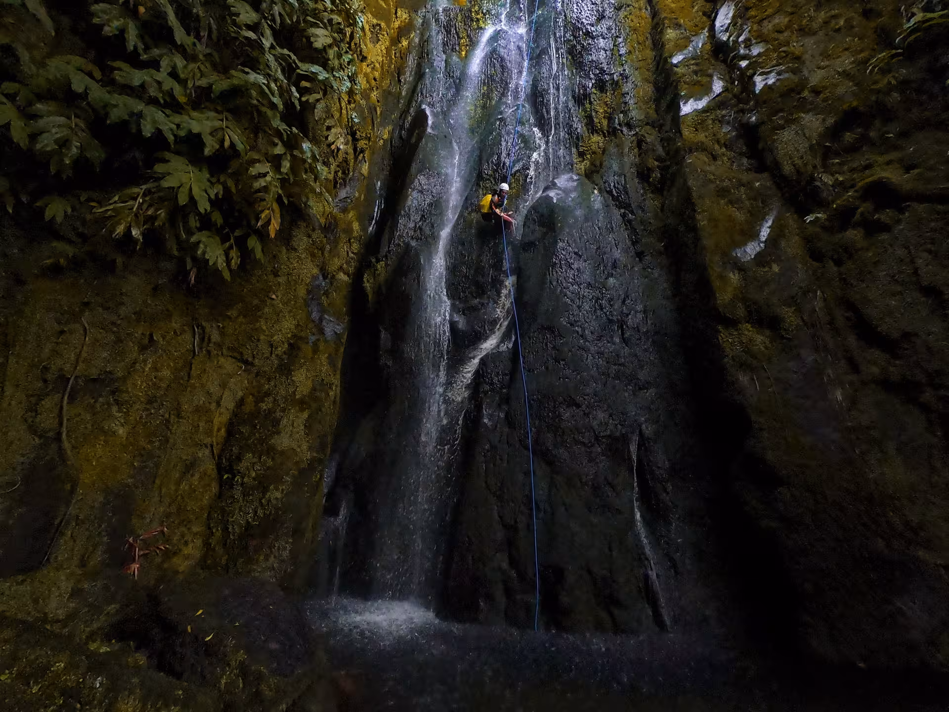Canyoning Lombadas Praia tour rappel down a rainforest waterfall into a dark volcanic canyon pool