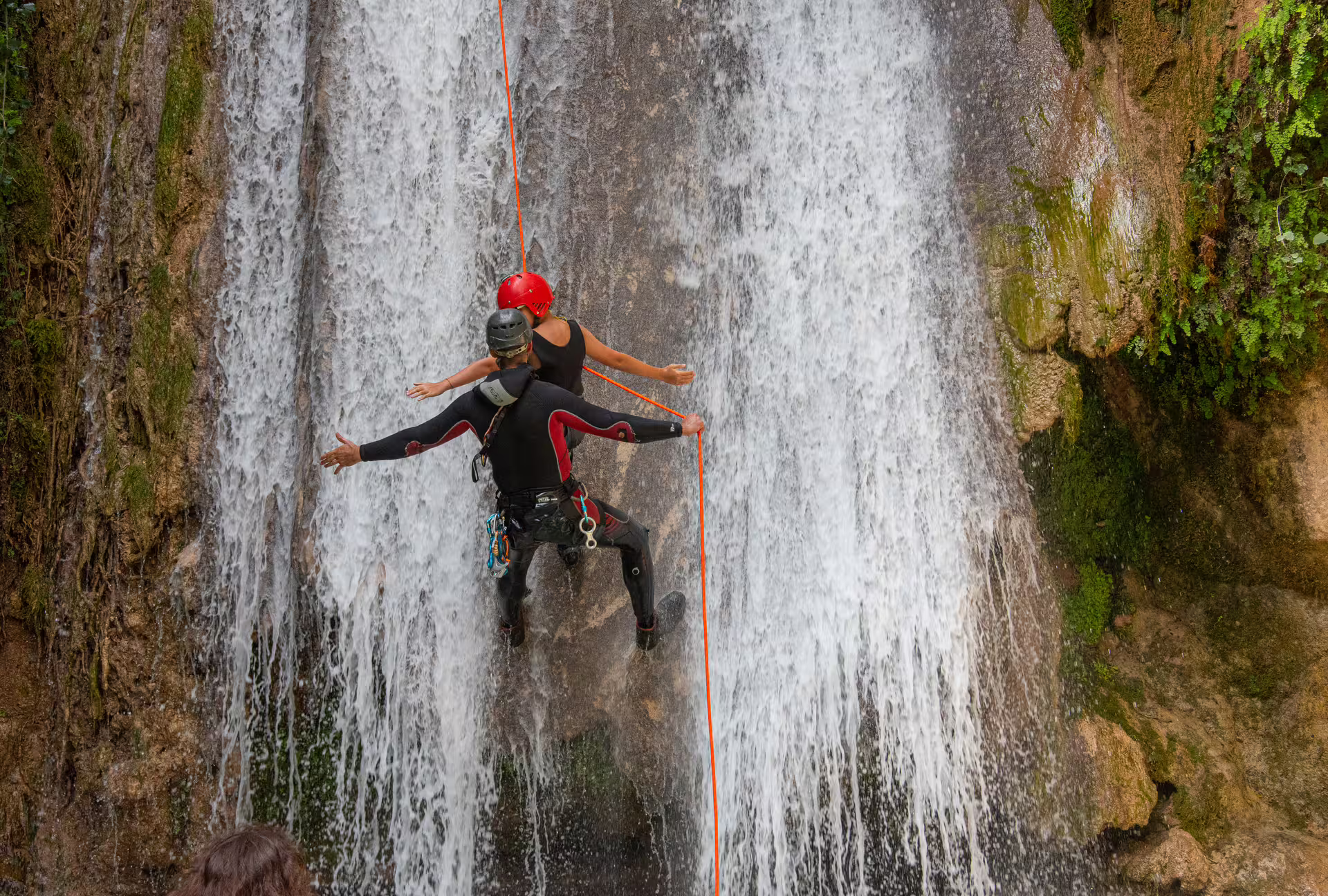 Guided canyoning rappel down Neda Waterfalls, Greece, climbers descending beside cascading water