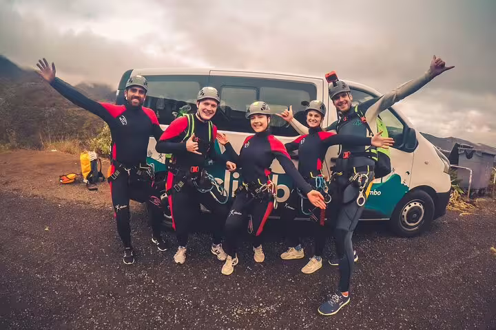 Group of excited canyoners in wetsuits and helmets pose in front of a van, ready for a rainforest adventure.
