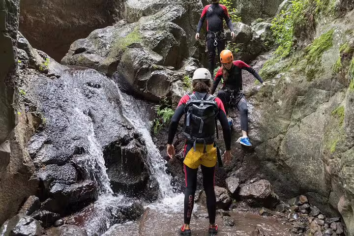 Group of canyoners navigating through rocky terrain and waterfalls in a vibrant rainforest setting, perfect for adventure seekers.