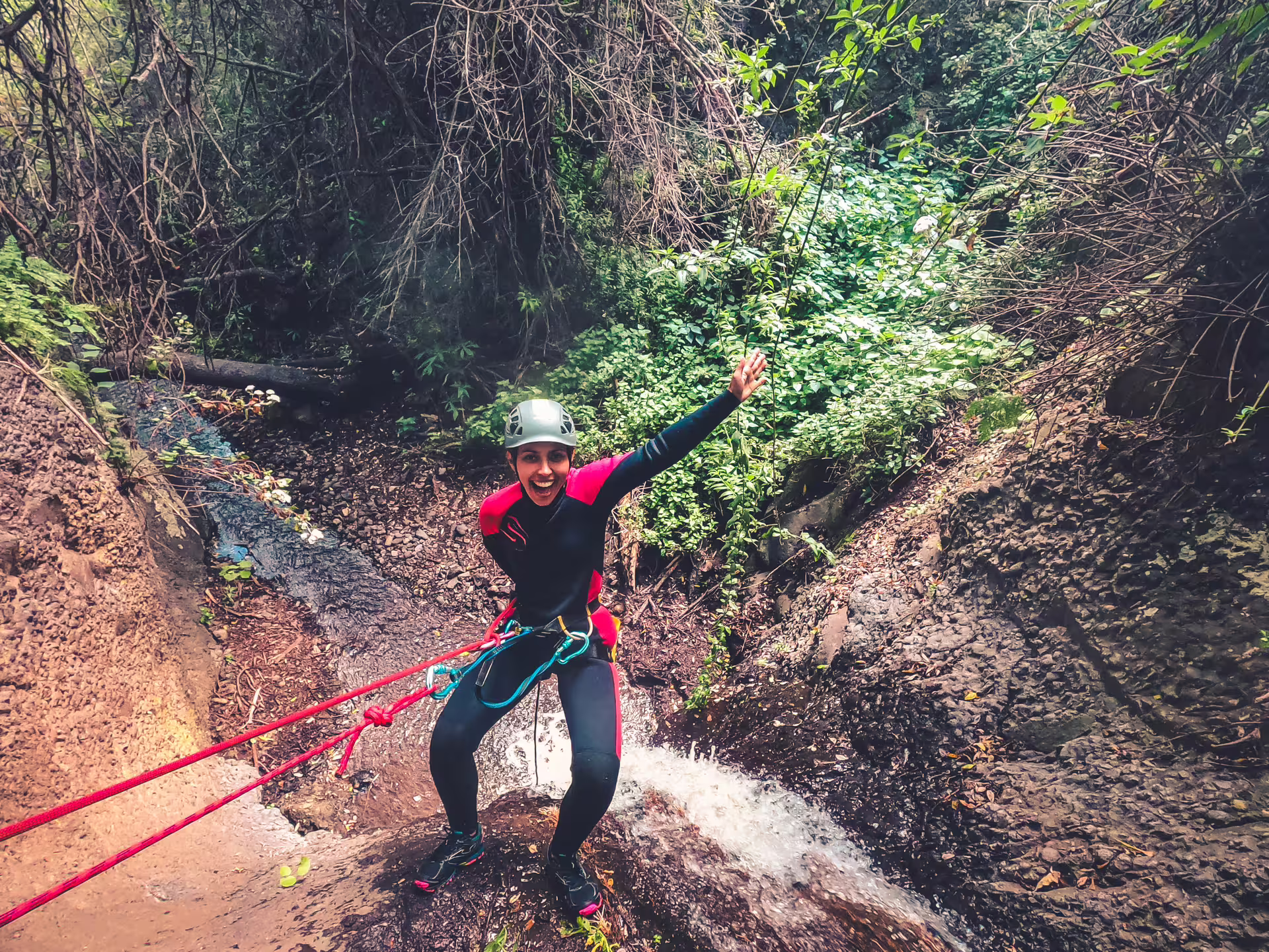 Excited canyoner descending a waterfall in vibrant rainforest, showcasing the thrill of canyoning adventures.