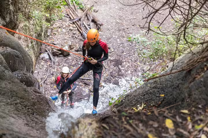 Two thrill-seekers navigate a steep waterfall descent in a rainforest, showcasing the excitement of canyoning adventures.