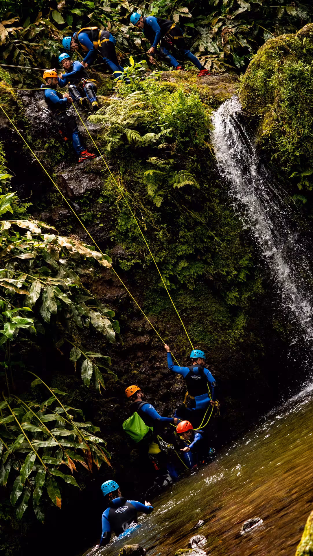 Guided canyoning group abseiling a mossy waterfall in Ribeira dos Caldeirões, São Miguel, with transport