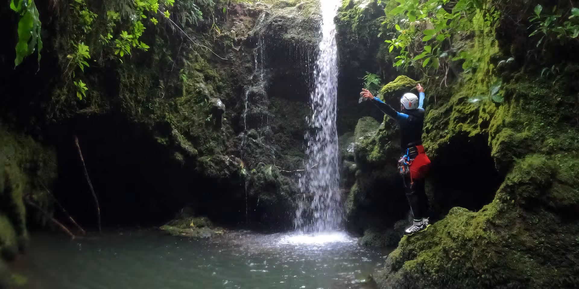 Canyoning Outward Shore jumper at jungle waterfall pool, ready for cliff jump in a scenic canyon gorge