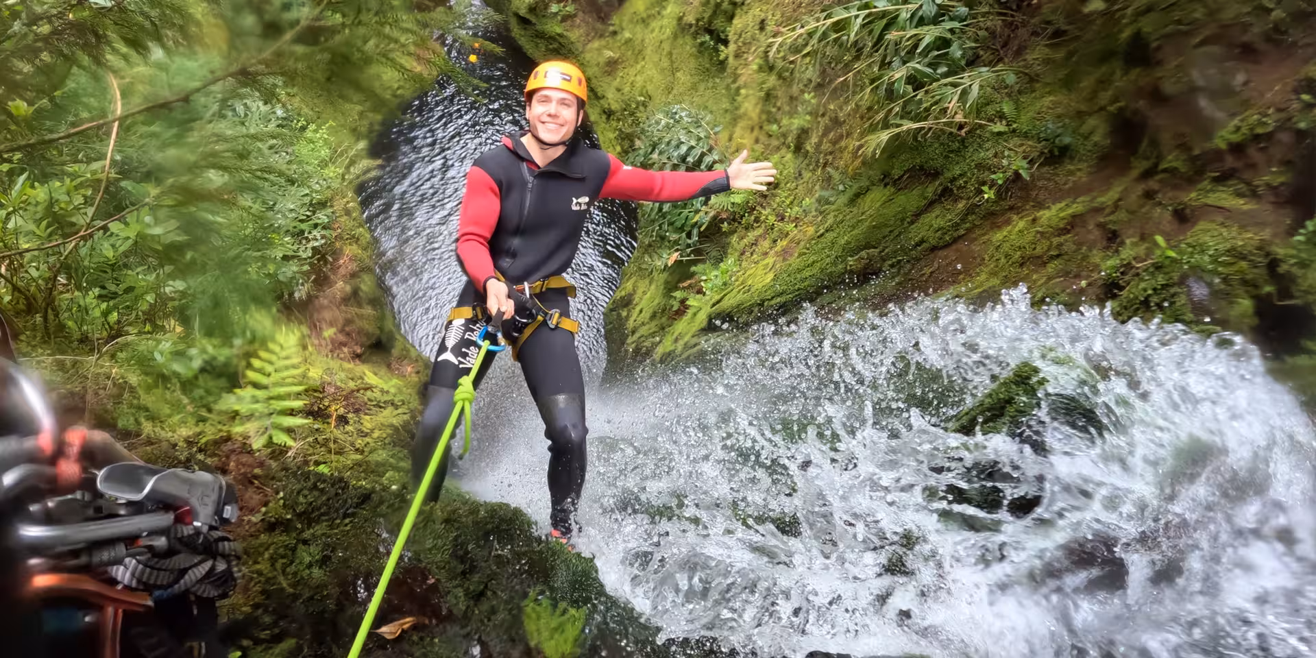 Smiling guide abseils beside a rushing waterfall in lush canyon on CANYONING Outward Shore adventure tour