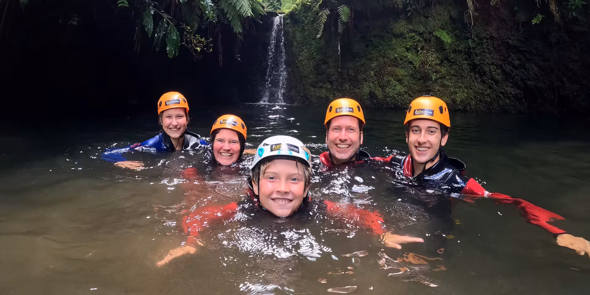 Canyoning Outward Shore group swims in a natural pool below a waterfall, helmets and wetsuits on tour