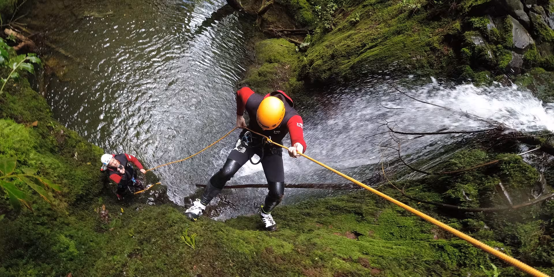 Canyoning Outward Shore rappel down mossy waterfall cliff with guide support, rope descent into clear pool