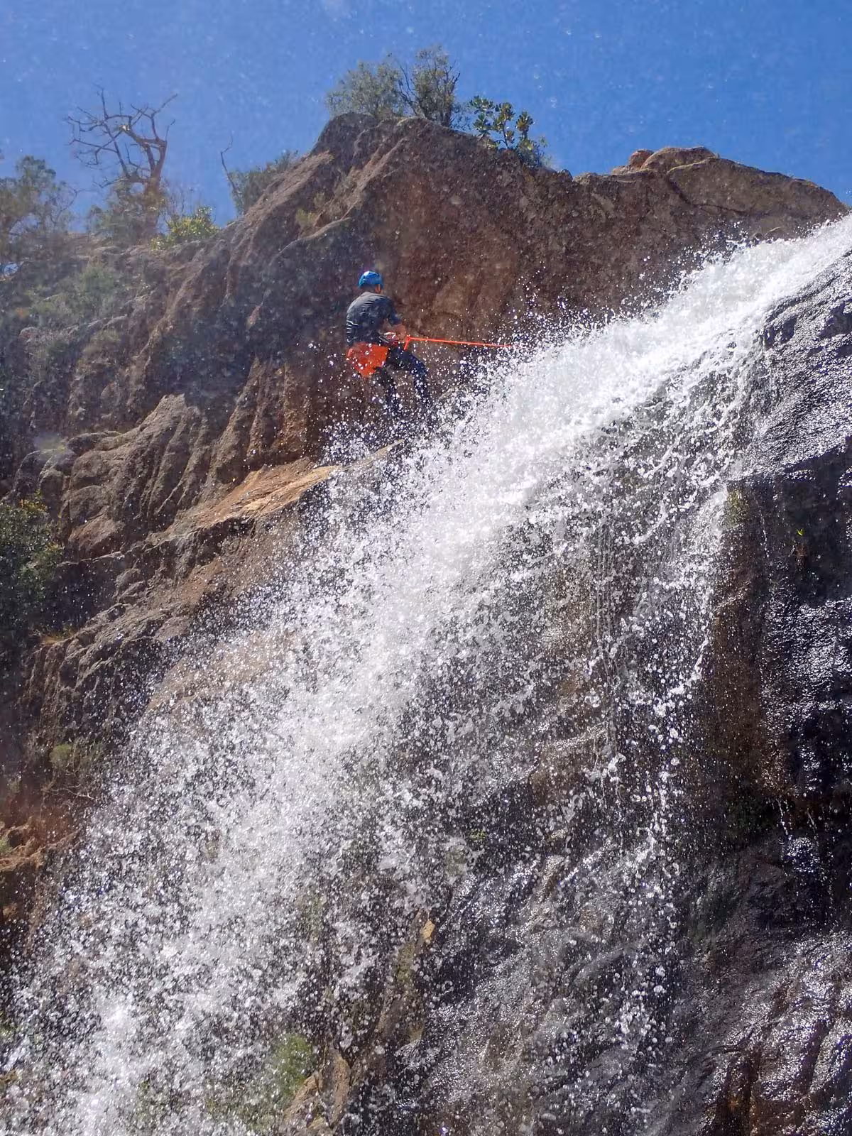 Adventurer descending a waterfall during canyoning in Rio Pitrisconi, San Teodoro, showcasing thrill and natural beauty.