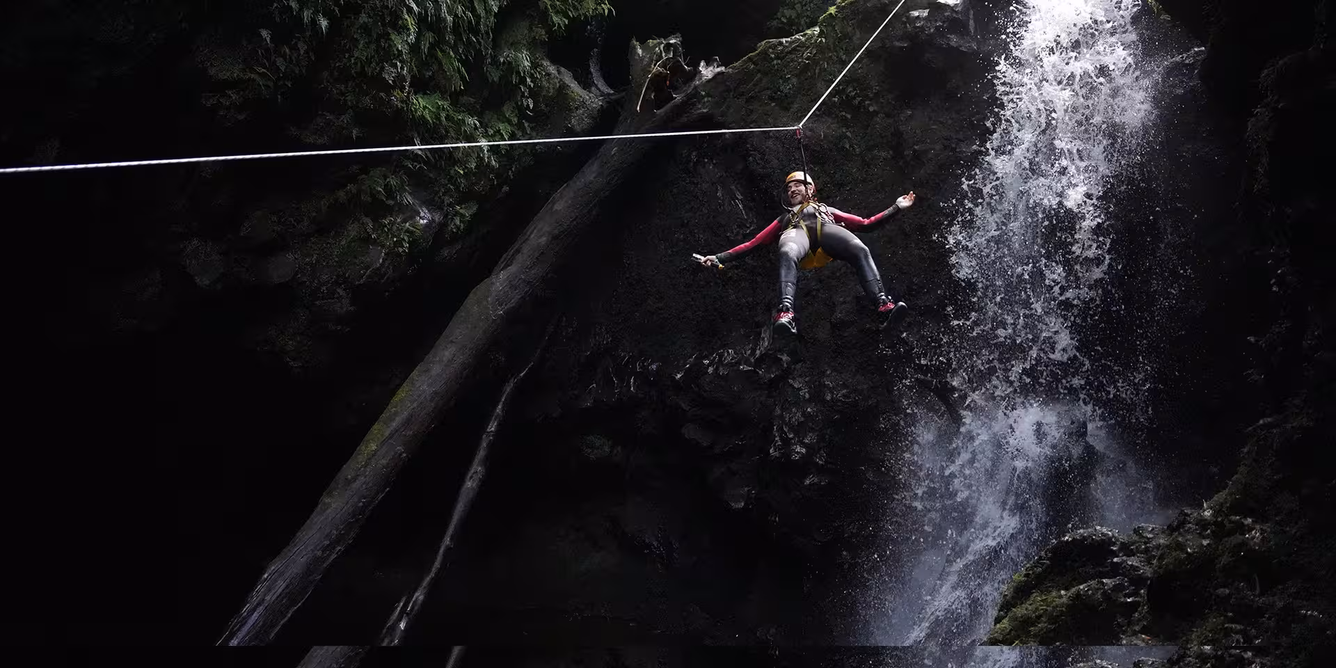 Canyoning tour rope swing above a waterfall, adventurer in helmet and wetsuit in a rocky canyon
