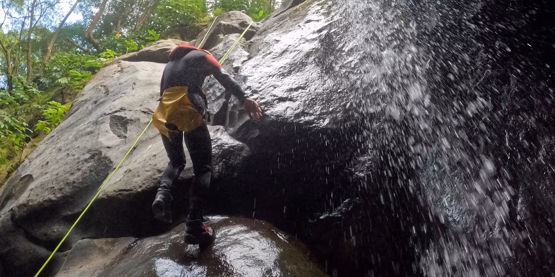 Canyoning at Salto do Cabrito as an adventurer climbs wet volcanic rock beside a rushing waterfall spray