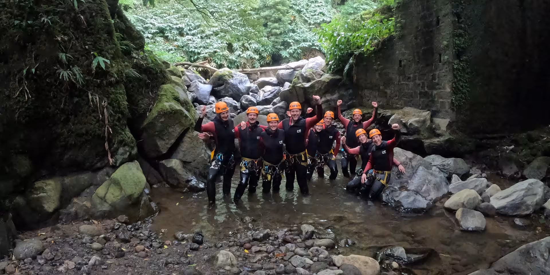 Group in wetsuits and helmets celebrating in a rocky Azores gorge on Salto do Cabrito canyoning tour