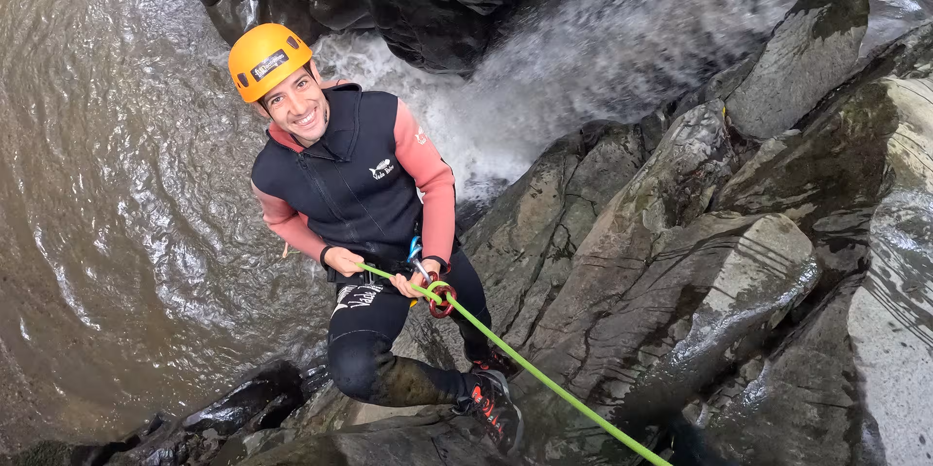 Canyoning at Salto do Cabrito: climber in helmet rappels down wet rocks beside a rushing waterfall