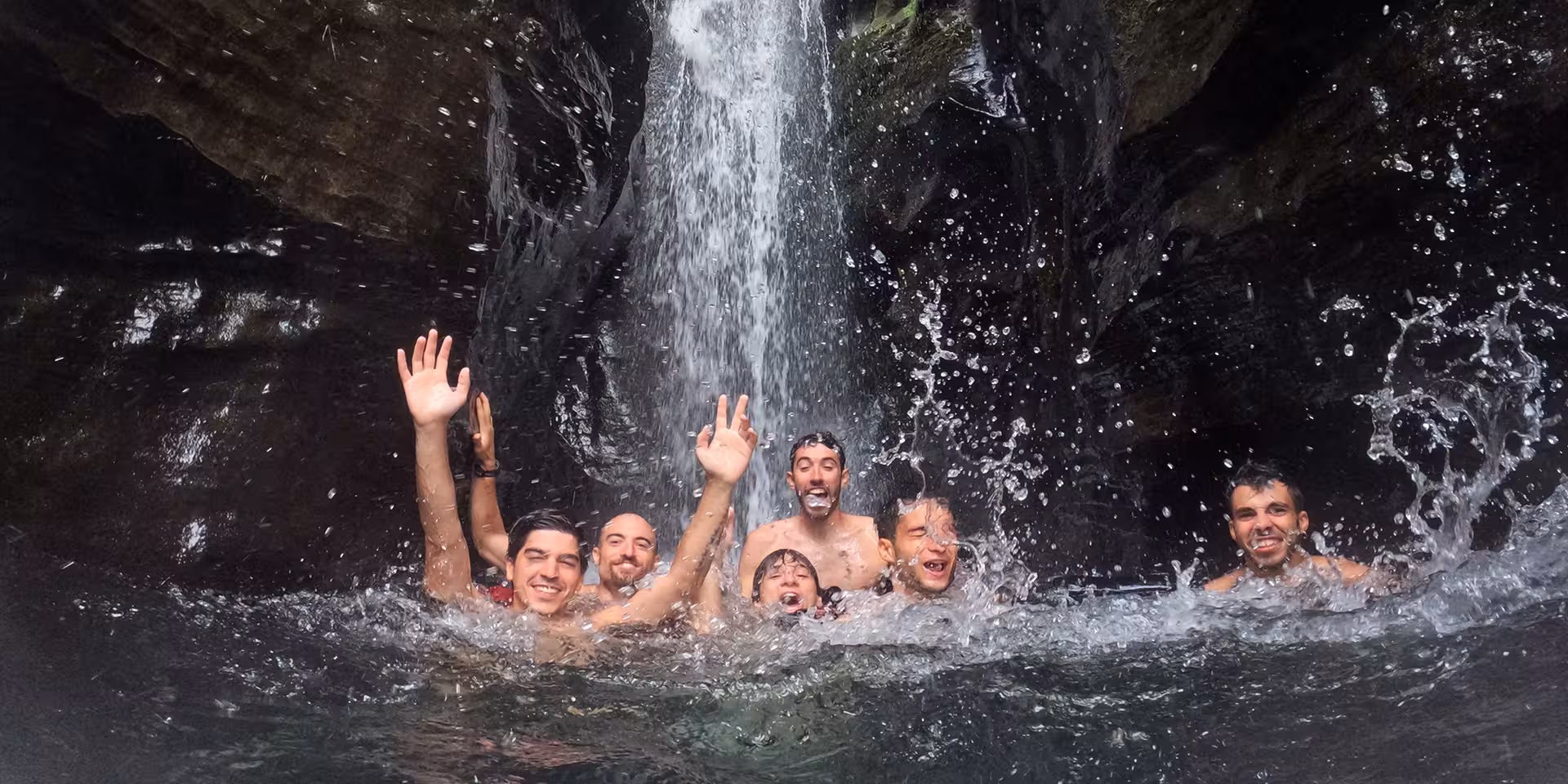 Canyoning tour swimmers cheering under Salto do Cabrito waterfall pool in São Miguel, Azores