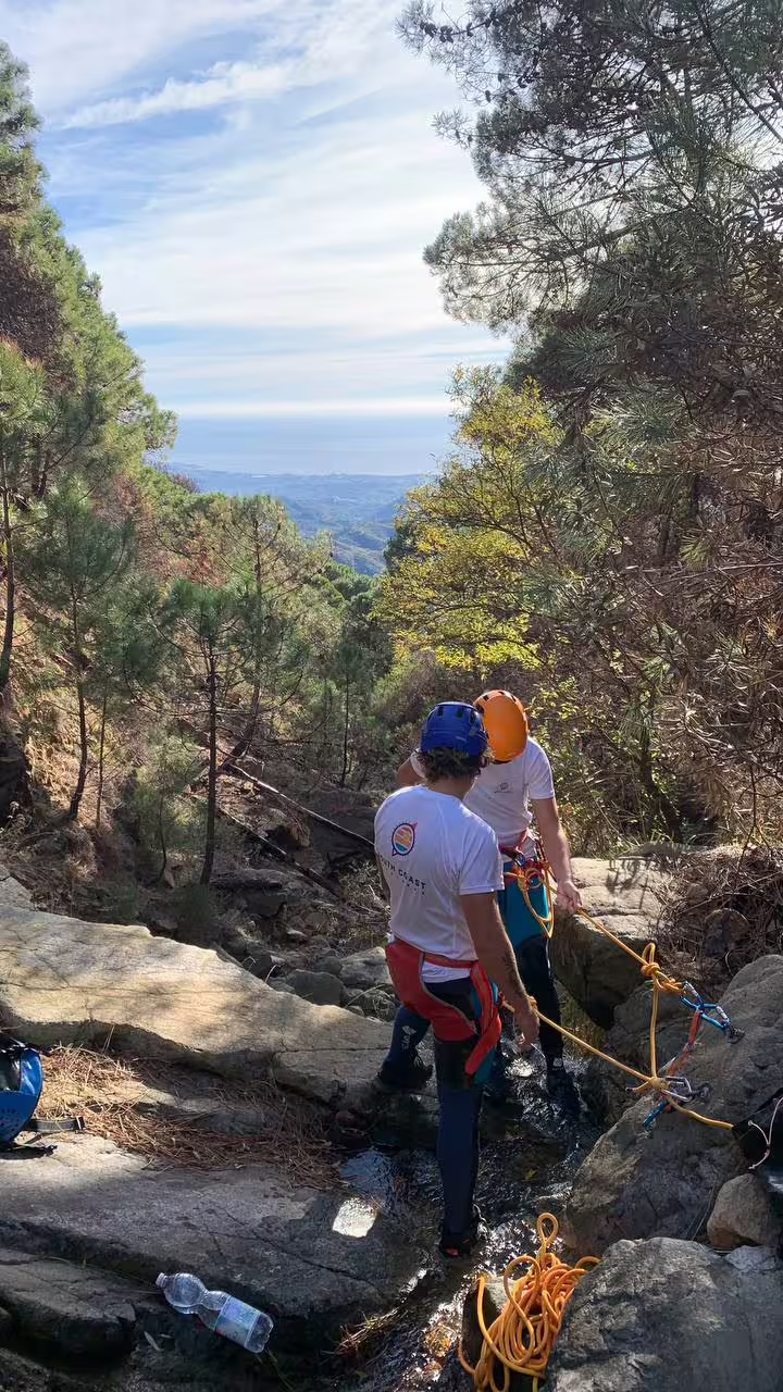 Two adventurers preparing ropes for canyoning with a stunning view of Sierra Bermeja and Estepona coastline.