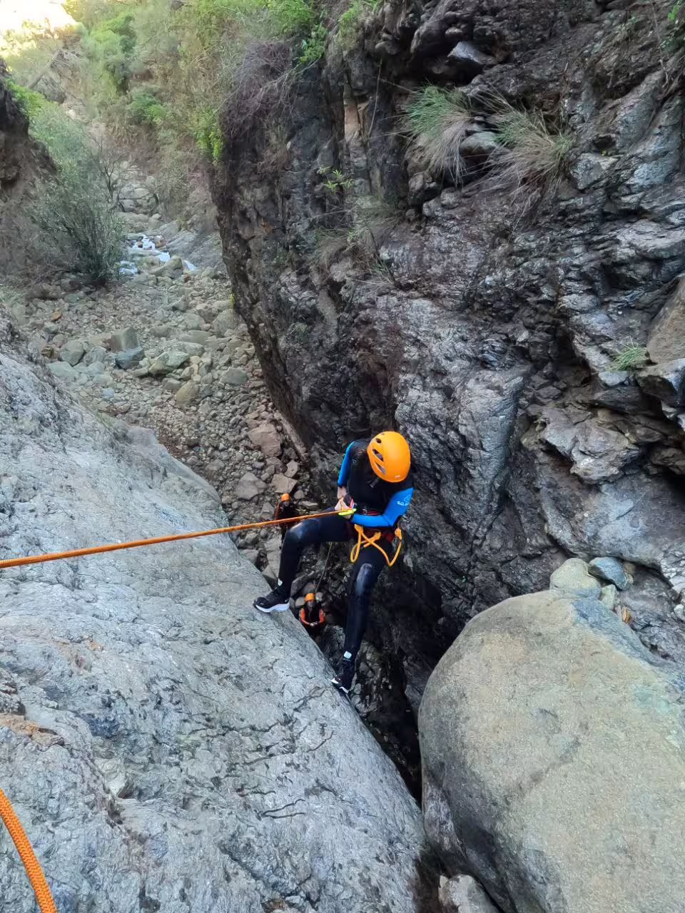 Canyoner descending a rugged rock face in Sierra Bermeja, Estepona, amidst a scenic mountain landscape.