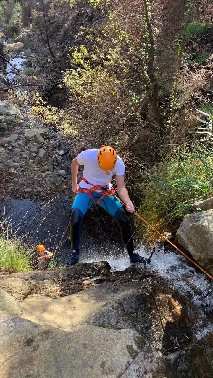 Adventurer rappels down a rocky waterfall amidst lush greenery in Sierra Bermeja, Estepona canyoning experience.