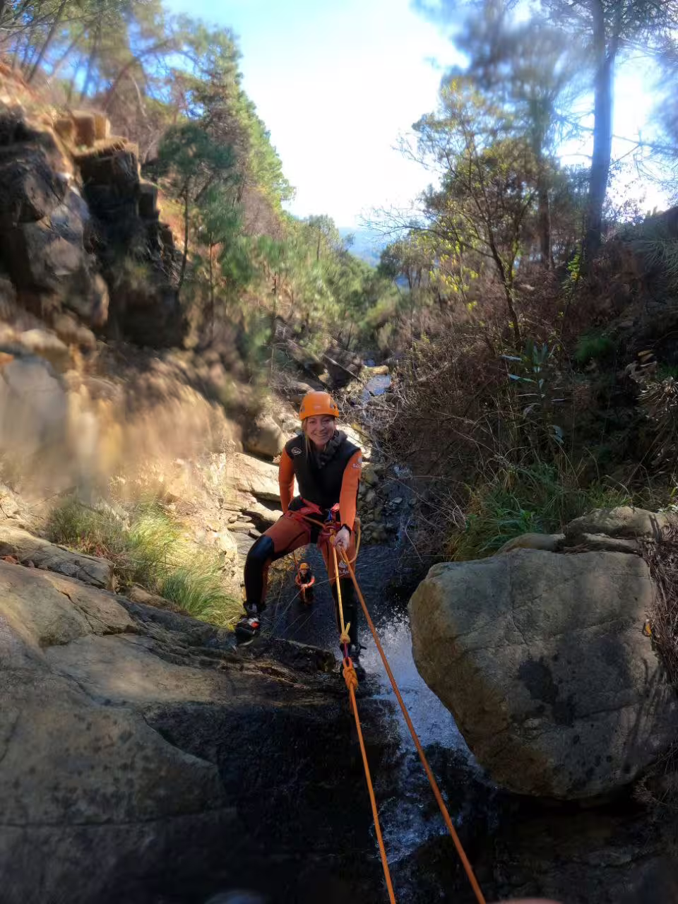 Adventurer rappelling down a rocky waterfall in Sierra Bermeja, Estepona, surrounded by lush greenery.