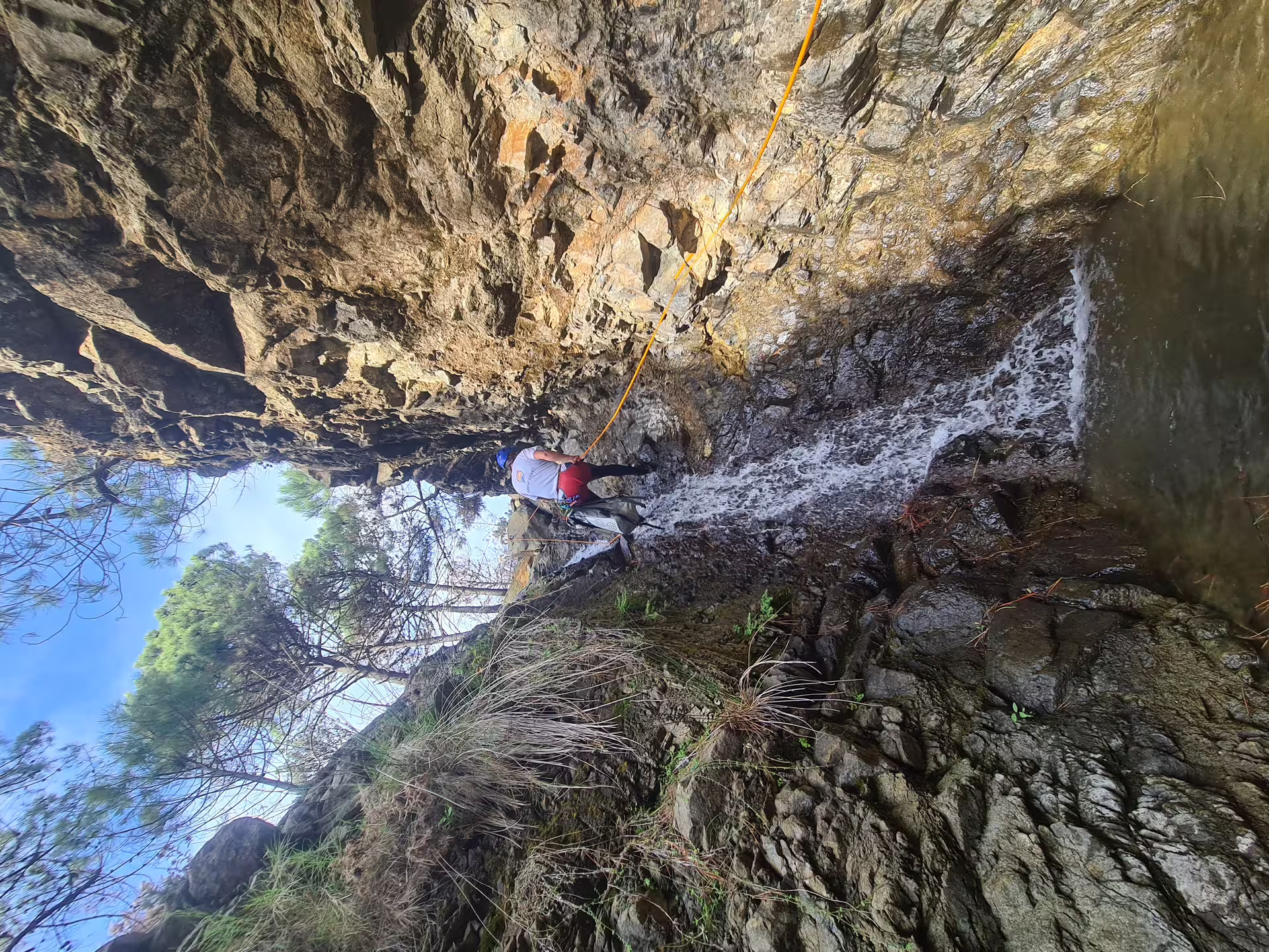 Canyoning enthusiasts maneuvering down a rocky waterfall in Sierra Bermeja, Estepona, amidst lush landscapes.