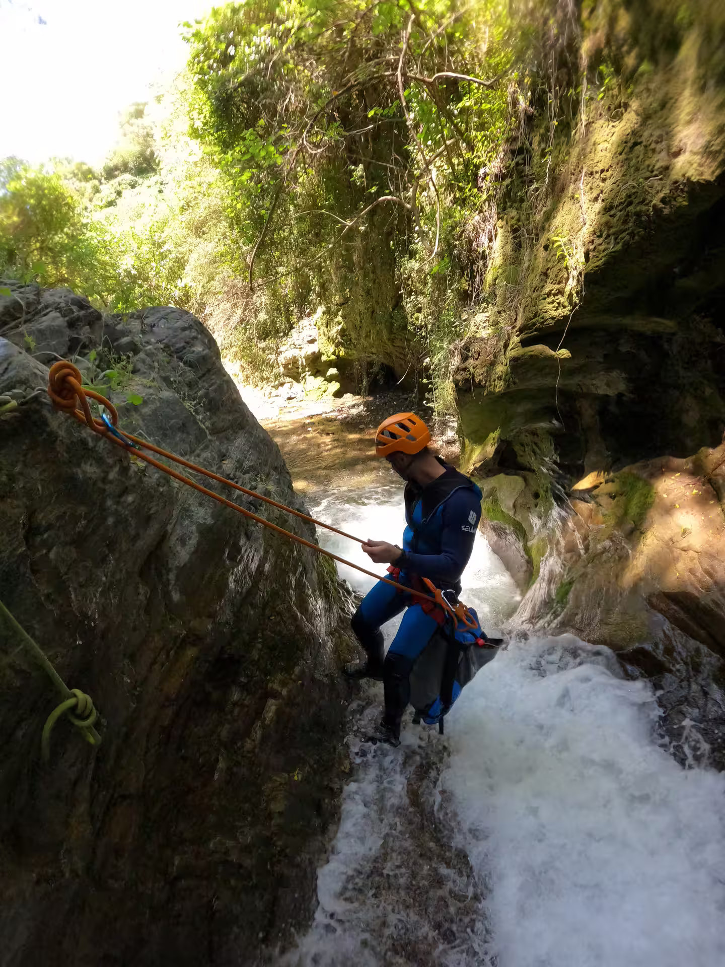 Adventurer canyoning down a waterfall in Sima del Diablo, near Estepona, surrounded by lush greenery and rugged rocks.