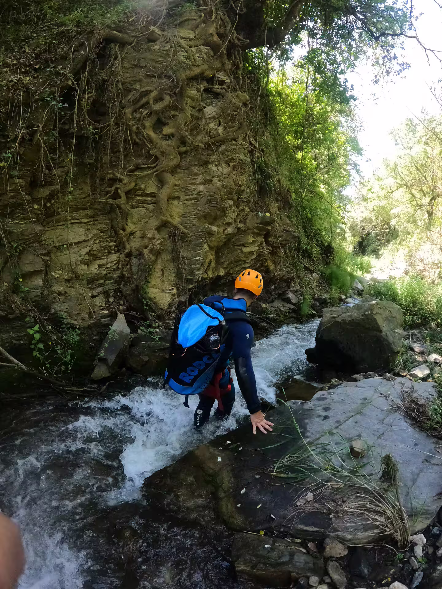 Adventurer in a wetsuit and helmet canyoning through rocky waters at Sima del Diablo near Estepona, surrounded by lush greenery.