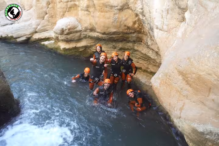 Group canyoning in Teruel swimming through a narrow limestone gorge pool with helmets and wetsuits