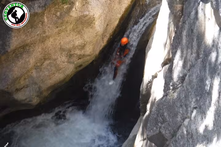 Canyoning Teruel rappel down narrow waterfall chute between rocks, guided canyon descent with helmet and wetsuit