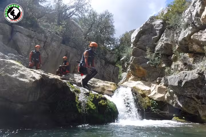 Adventure canyoning in Teruel as participants jump into a turquoise pool below a small waterfall in a rocky canyon
