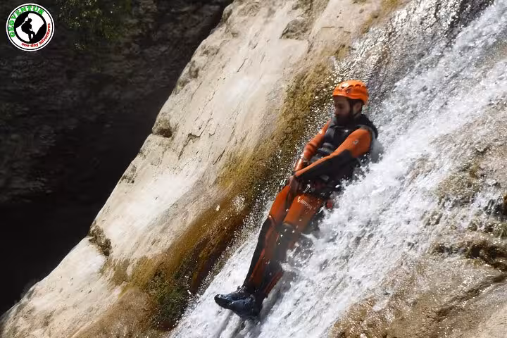 Canyoning in Teruel as a participant slides down a natural waterfall chute in wetsuit, helmet and harness