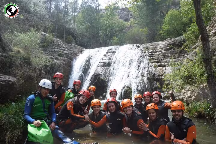 Group canyoning tour in Teruel posing in wetsuits and helmets by a waterfall pool, adventure activity in Spain