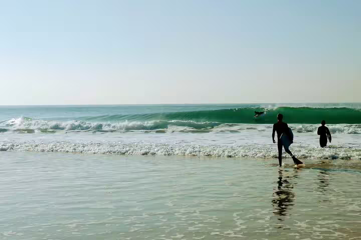 People in wetsuits prepare to bodyboard on Caparica Beach, enjoying perfect waves and sunny skies for an adventurous day.