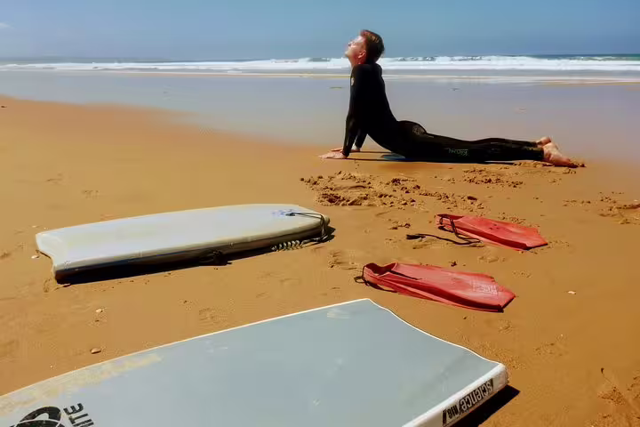 Person stretching on Caparica beach with bodyboards and fins, perfect for an exhilarating bodyboarding adventure in Portugal.