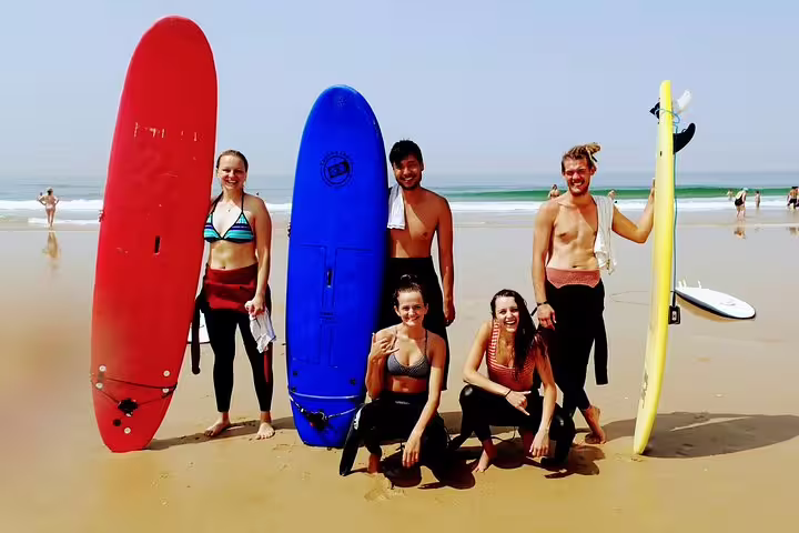 Group of happy surfers with colorful boards enjoying the Caparica Surf Experience on a sunny beach day in Portugal.