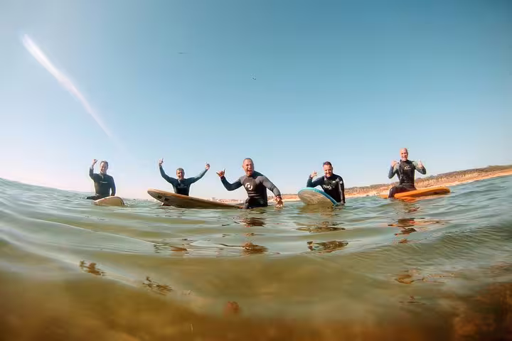 Group of surfers enjoying the Caparica Surf Experience, riding waves under clear skies with vibrant energy and excitement.